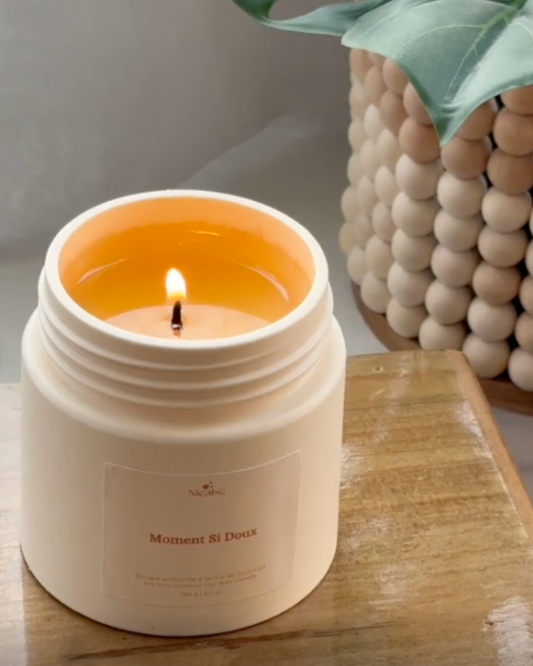 Bougie parfumée Nicaise « Moment Si Doux » allumée dans son pot blanc, posée sur une table en bois.