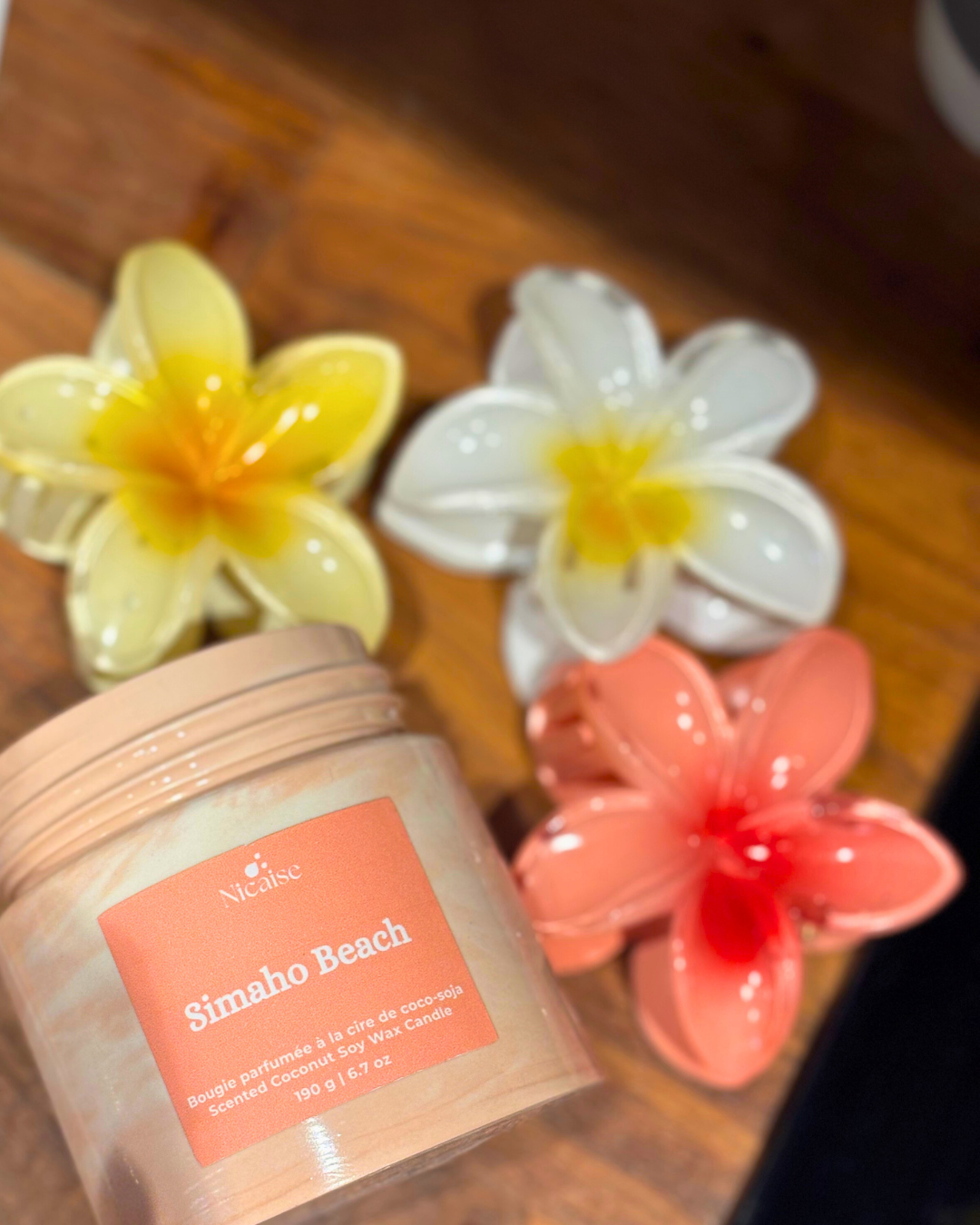 Bougie parfumée Nicaise « Simaho Beach » en pot corail marbré, posée sur table en bois avec fleurs décoratives.