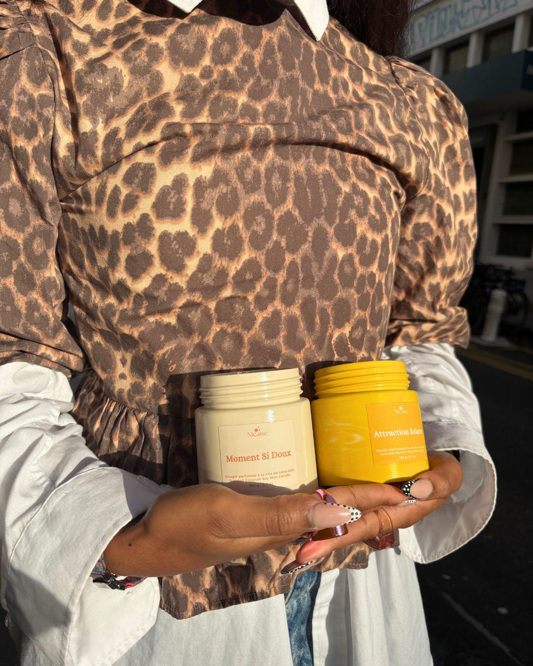 Deux bougies parfumées artisanales Nicaise en pots, Moment Si Doux (beige) et Attraction Solaire (jaune), tenues à la main.