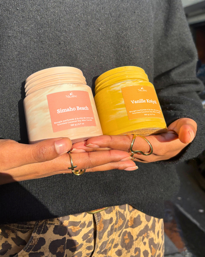 Deux bougies parfumées artisanales Nicaise en pots marbrés, Simaho Beach (beige) et Vanille Kréyòl (jaune), tenues à la main.