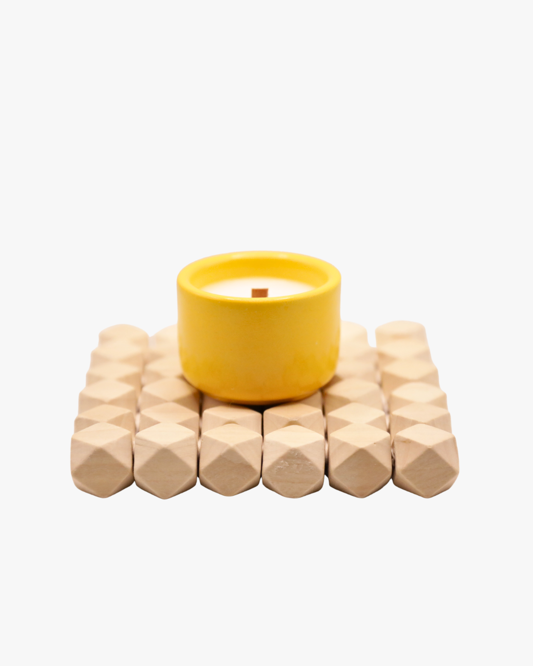 Mini bougie parfumée Nicaise « Attraction Solaire » en pot jaune avec mèche en bois, posée sur un support en bois, sur fond blanc.