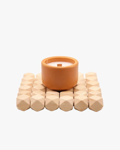 Mini bougie parfumée Nicaise « Délice Sucré » en pot marron avec mèche en bois, posée sur un support en bois, sur fond blanc.