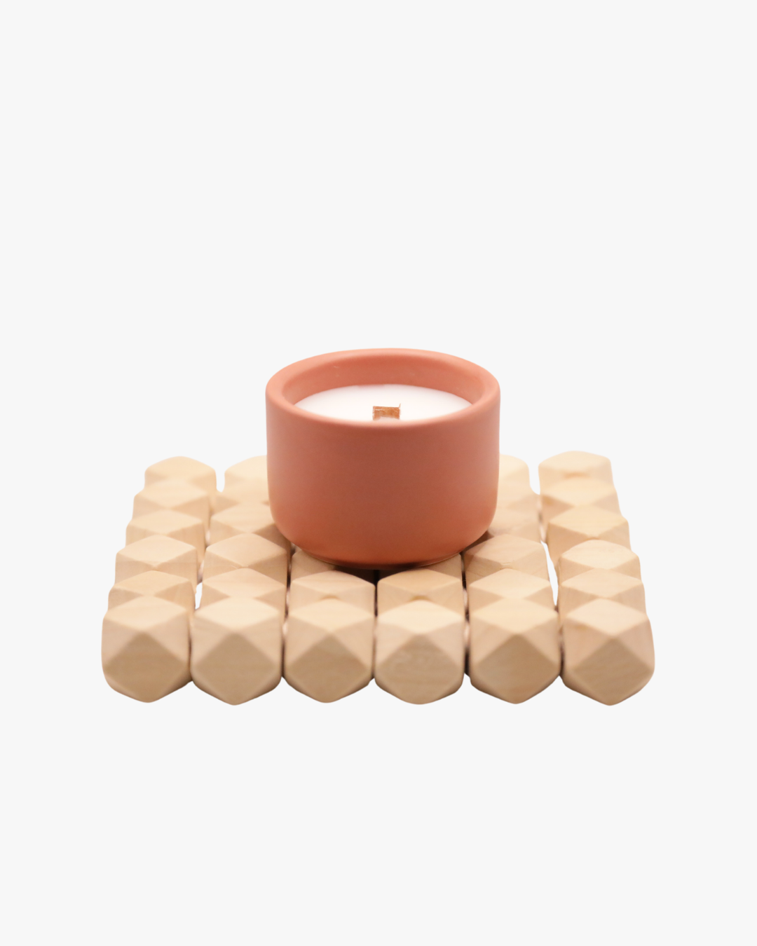 Mini bougie parfumée Nicaise « Simaho Beach » en pot rose avec mèche en bois, posée sur un support en bois, sur fond blanc.